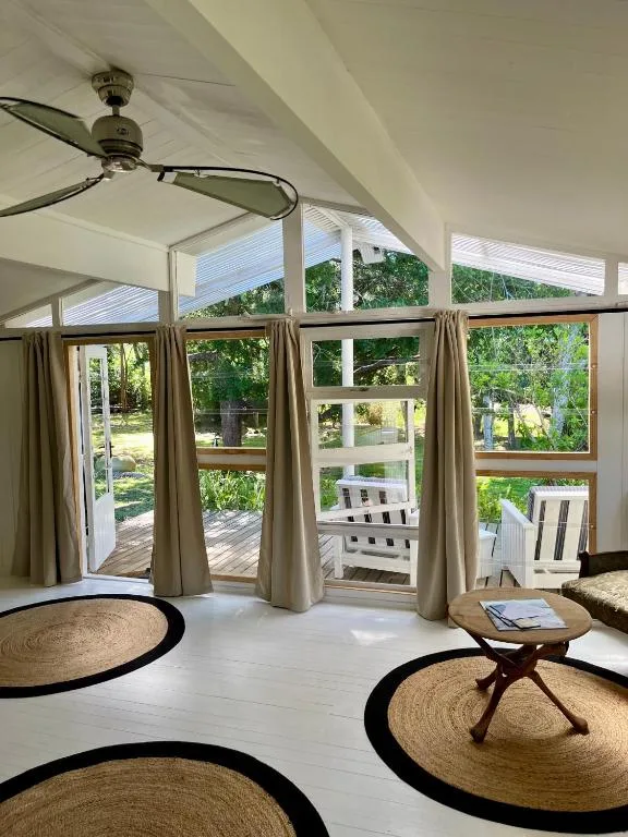 Bright lounge with ceiling fan, large windows overlooking garden and deck area