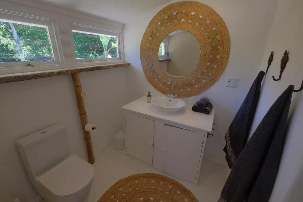 Bright bathroom with white vanity, woven mirror, and toilet fixtures