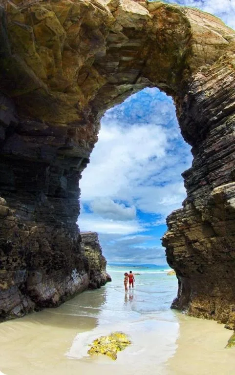 Rocky natural arch frames pristine beach and ocean beyond with swimmers