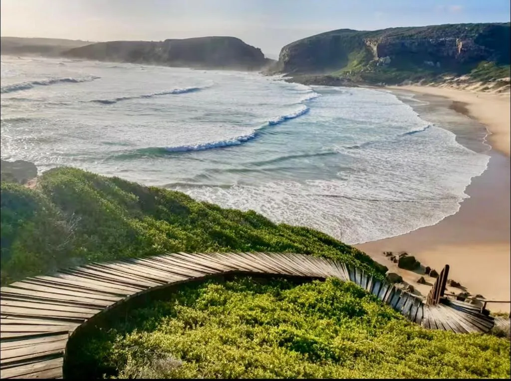 Scenic coastal beach with rolling waves, golden sand, and dramatic green cliffs