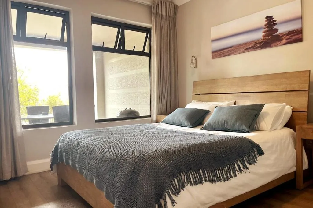 Bright bedroom with wooden bed frame and large windows overlooking garden