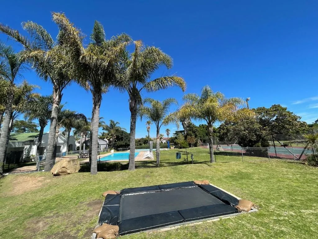 Spacious lawn with trampoline, palm trees, pool and tennis court visible