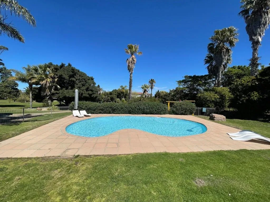 Kidney-shaped swimming pool with surrounding patio and manicured gardens under clear blue sky