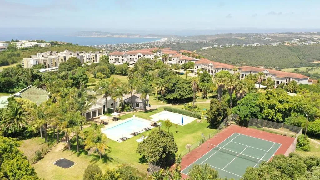Aerial view of property with pool, tennis court, and coastal landscape beyond