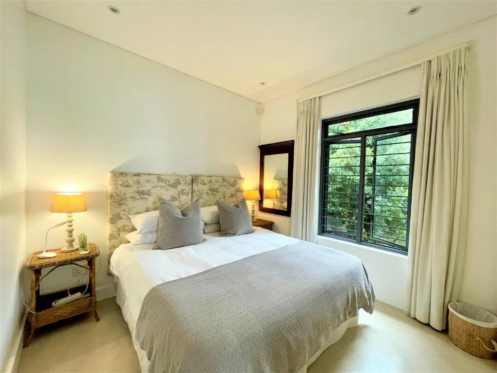 Bright bedroom with queen bed, patterned headboard, garden views through glass doors