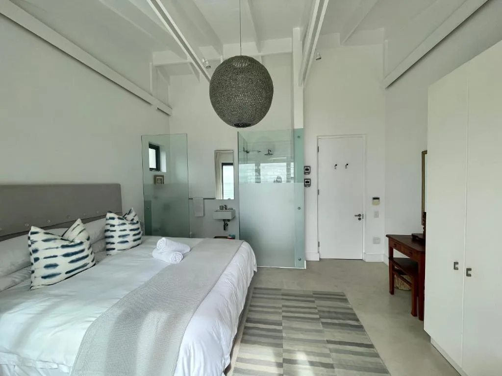 Modern bedroom with queen bed, en-suite bathroom visible behind glass partition