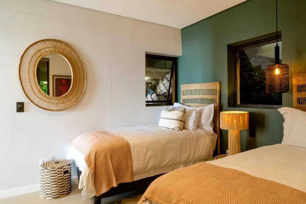 Contemporary bedroom with twin beds, woven mirror, and green accent wall