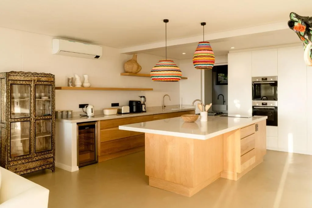 Modern open-plan kitchen with wooden island, white counters, and colorful pendant lights