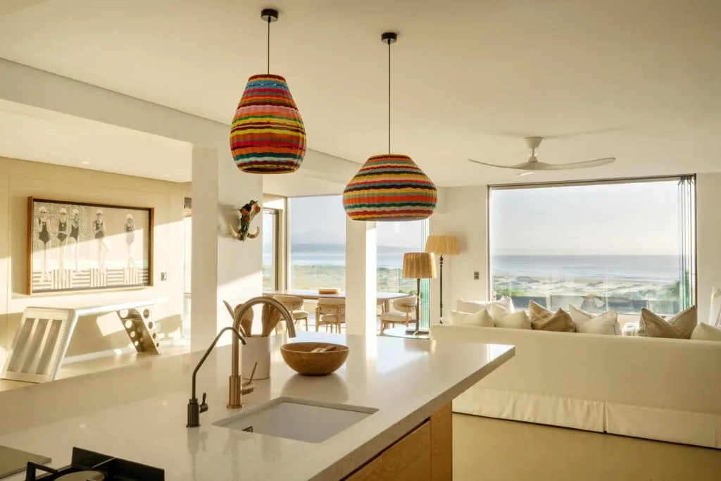 Open-plan lounge with ocean views, colorful pendant lights, and coastal decor