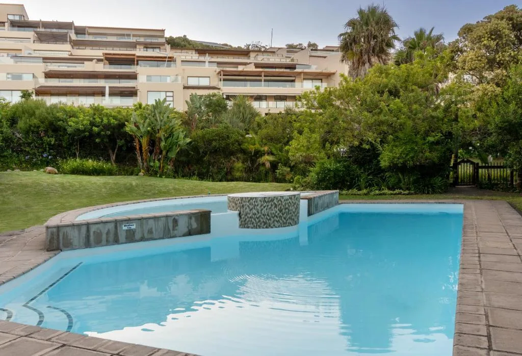 Inviting turquoise swimming pool with spa area and lush gardens beyond