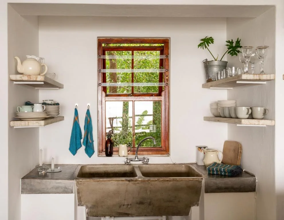 Rustic bathroom with double basin sink and wooden-framed window overlooking garden