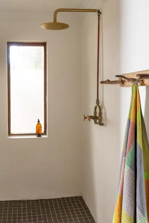 Modern bathroom with brass rainfall shower, mirror, and colorful towels