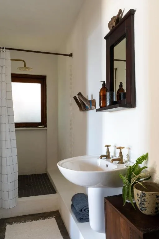 Modern bathroom with white pedestal sink, black-framed mirror, and shower area