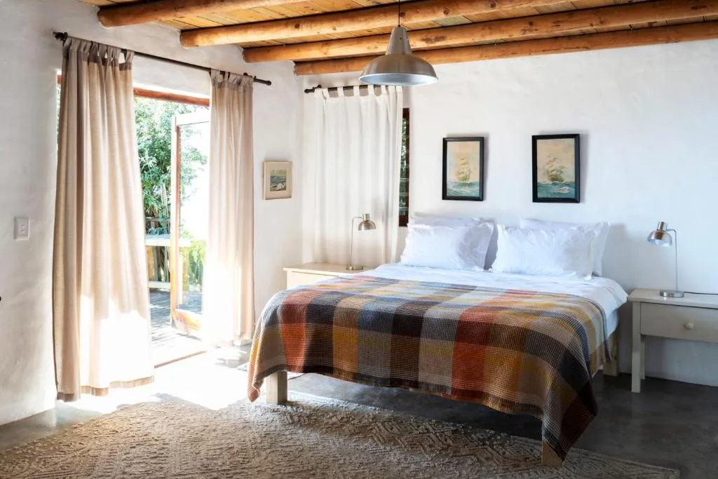 Bright bedroom with queen bed, wooden beams, and garden views through French doors