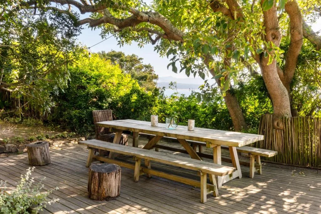 Wooden picnic table and benches on shaded deck with ocean view