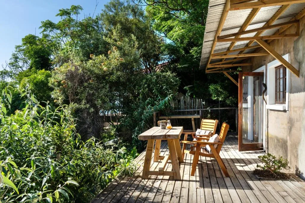 Wooden deck with dining table and chairs, surrounded by lush garden vegetation