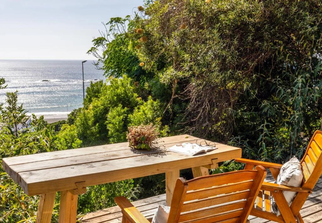 Wooden deck with table and chairs overlooking ocean and coastal vegetation