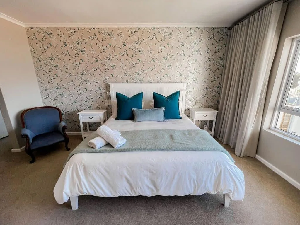 Spacious master bedroom with white bed, teal pillows, and floral wallpaper