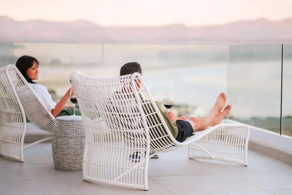 Guests relaxing on modern white chairs on spacious patio overlooking lagoon