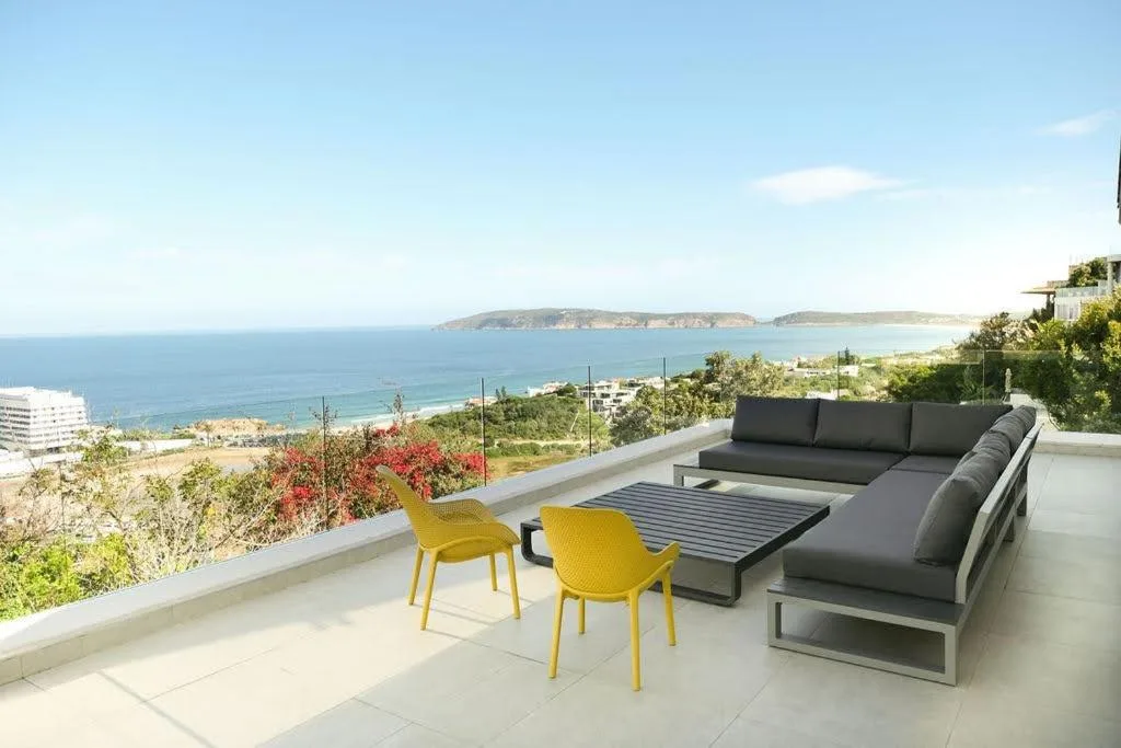 Modern patio with ocean view, gray sofa, yellow chairs, and coastal landscape