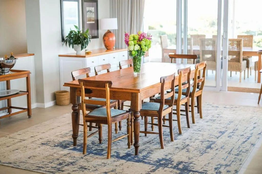 Spacious dining room with wooden table, chairs, fresh flowers, and garden views