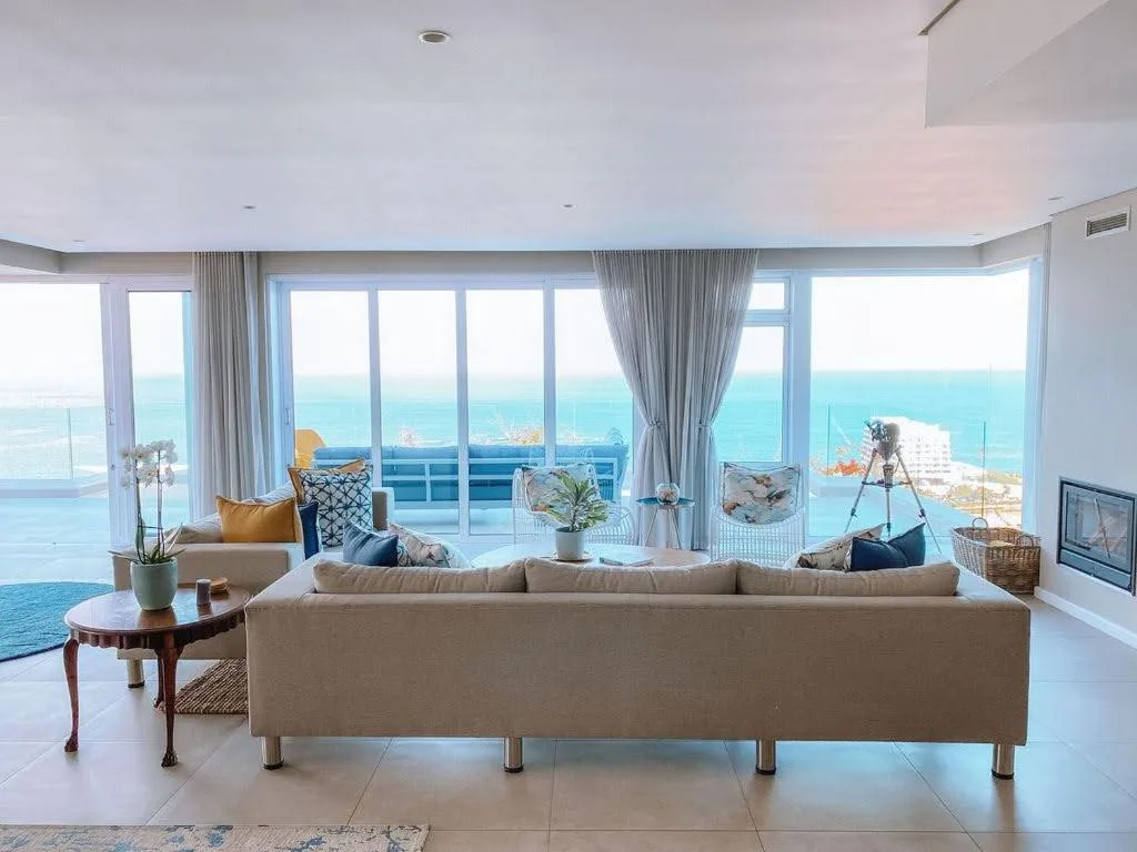 Spacious lounge with beige sofa overlooking turquoise ocean views through floor-to-ceiling windows