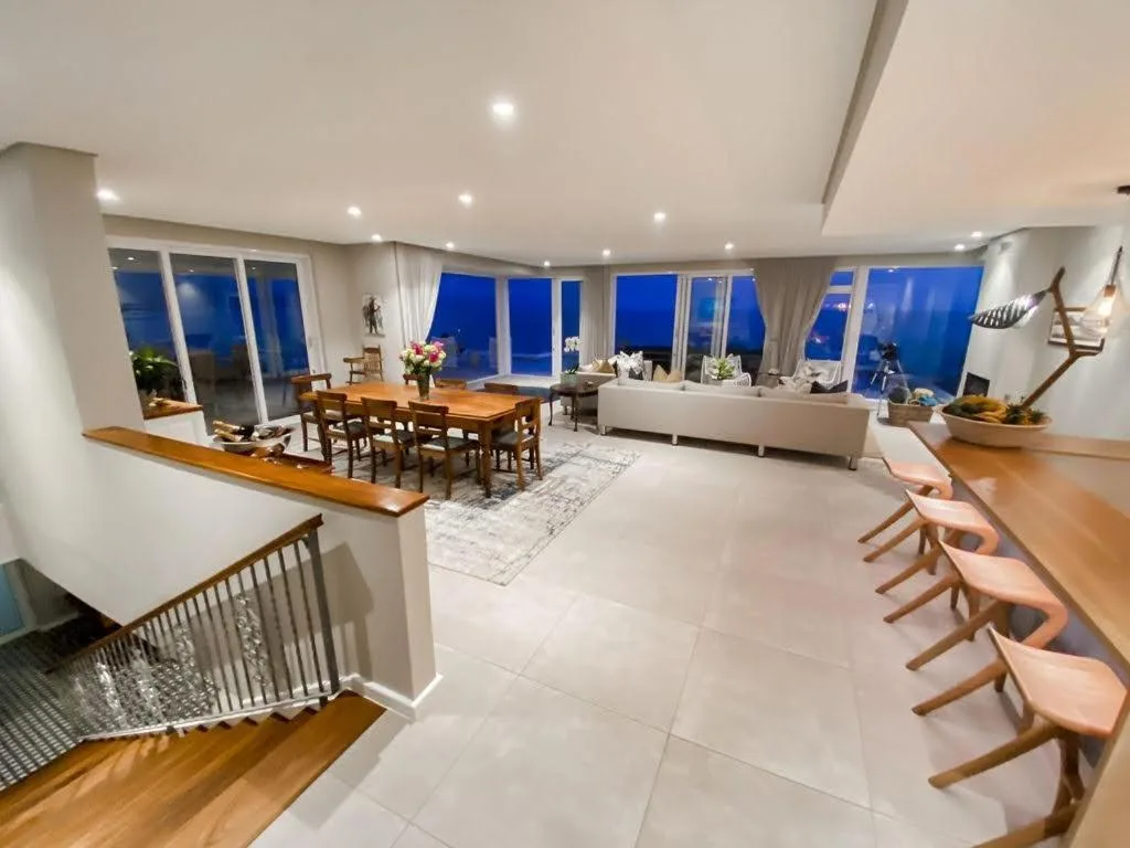Modern open-plan lounge with sea views, white sofa, wooden dining table, and floor-to-ceiling windows