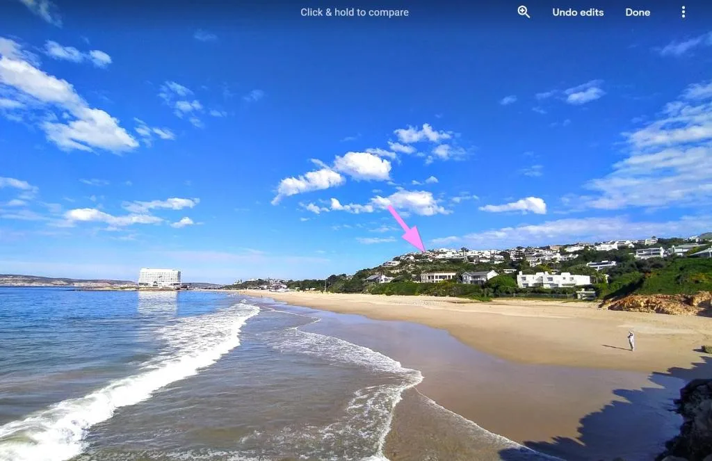 Sandy beach with ocean waves and cliffside homes under blue sky