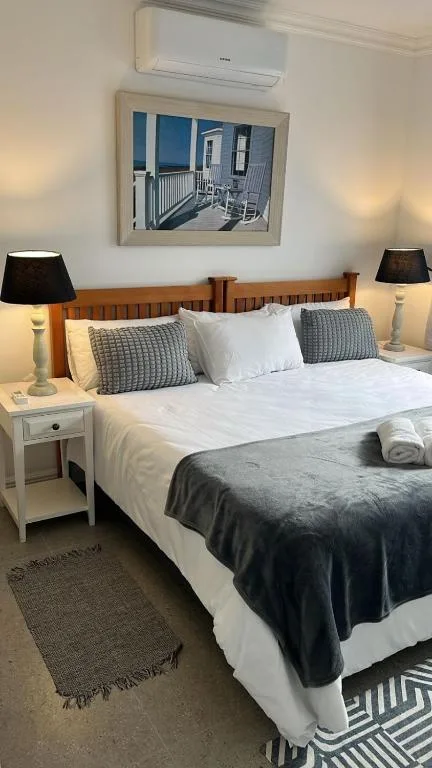 Neatly made bed with wooden headboard, white linens, decorative pillows, bedside lamps