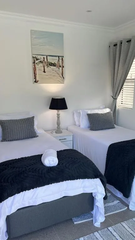 Twin bedroom with white bedding, black throws, beach artwork, and bedside lamp