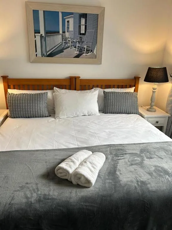 Neatly made bed with white pillows and rolled towels on gray bedding