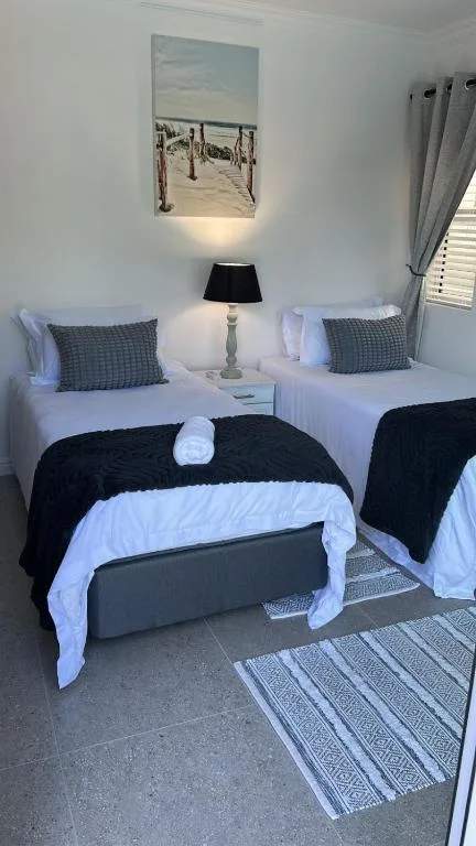 Twin bedroom with white bedding, dark throws, coastal artwork above