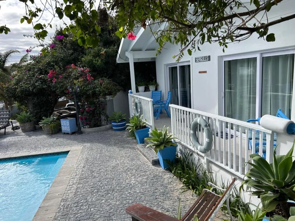 Seaside patio with pool, white railings, blue chairs, flowering plants