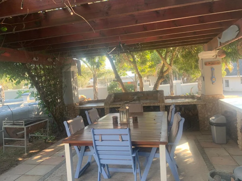 Covered patio area with dining table and blue chairs, shaded by trees