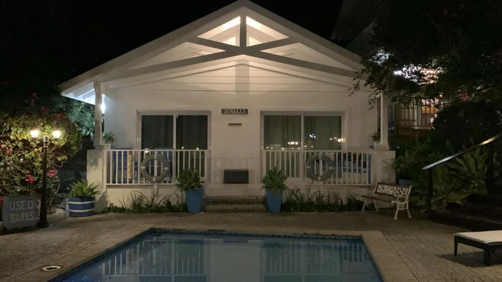 White cottage with pool at night, illuminated entrance and manicured garden