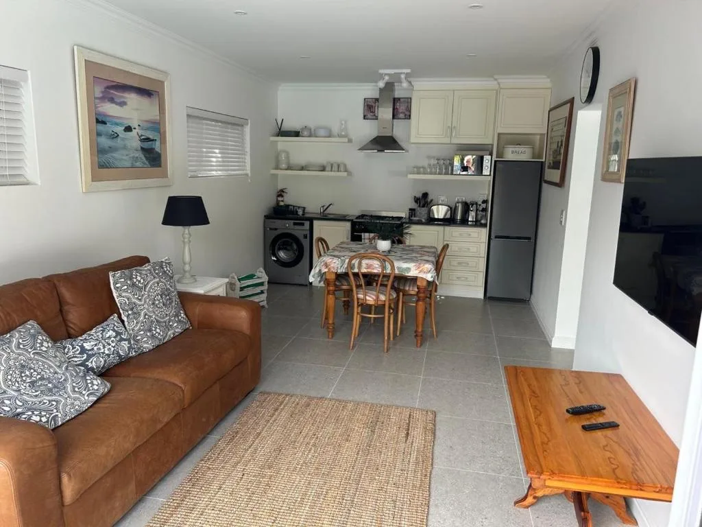 Open-plan living area with brown leather sofa and kitchen visible behind
