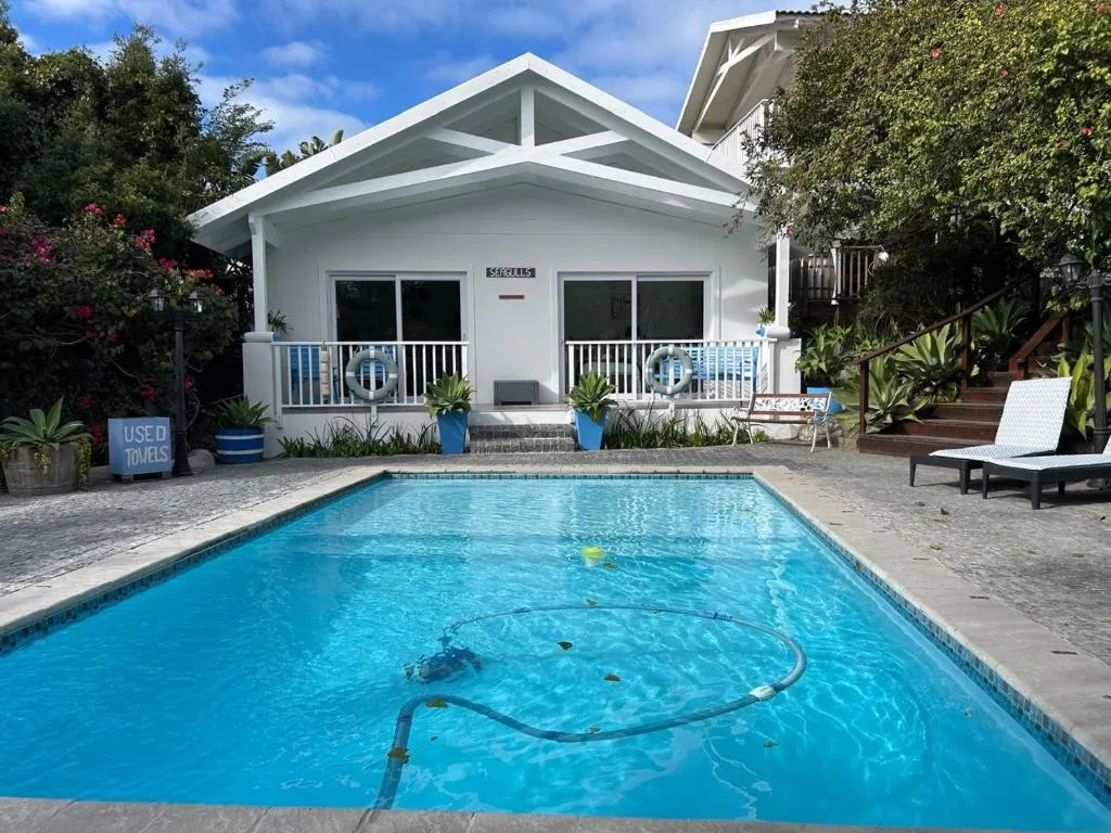 Sparkling blue swimming pool with white cottage and garden surroundings