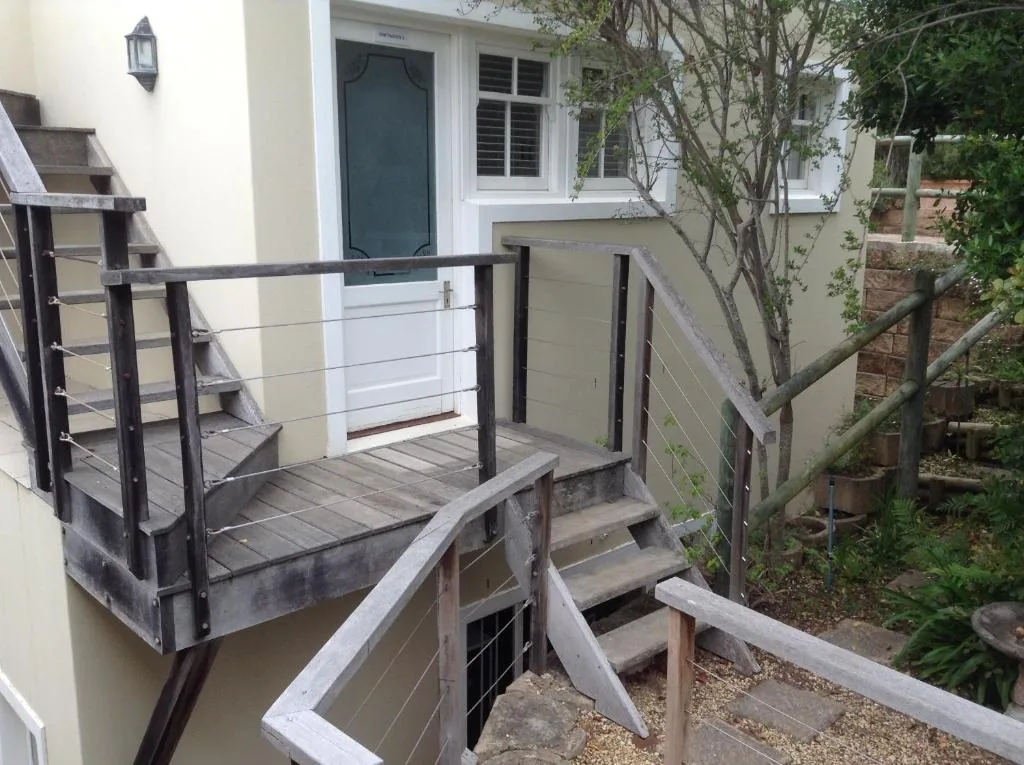 Modern entrance with dark railings, stairs, and lush green garden surroundings