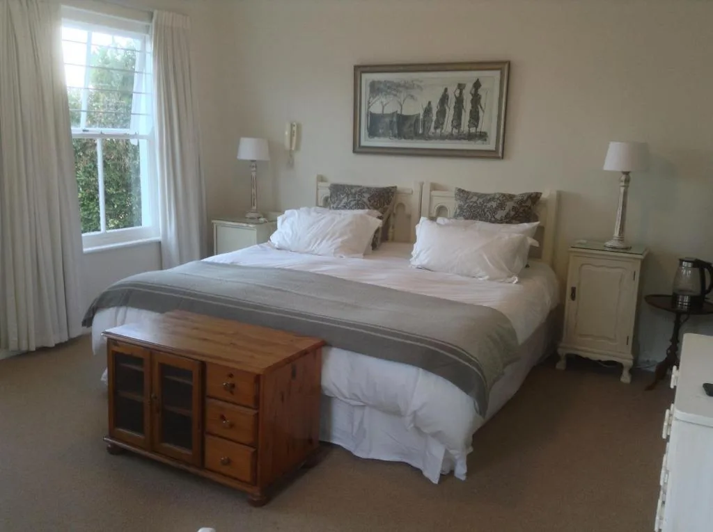 Spacious bedroom with queen bed, neutral furnishings, and garden views through windows