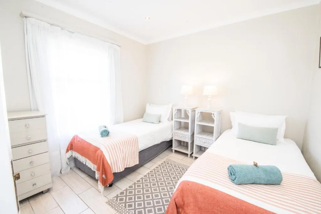 Bright bedroom with two single beds, white walls, and natural light from window
