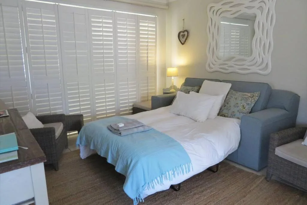 Bright bedroom with queen bed, white shutters, decorative mirror, and lounge seating
