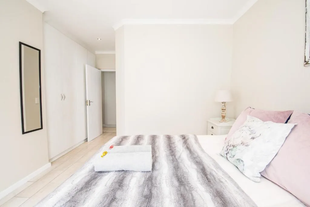 Bright bedroom with striped bedding, pink pillows, white cabinetry, and mirror
