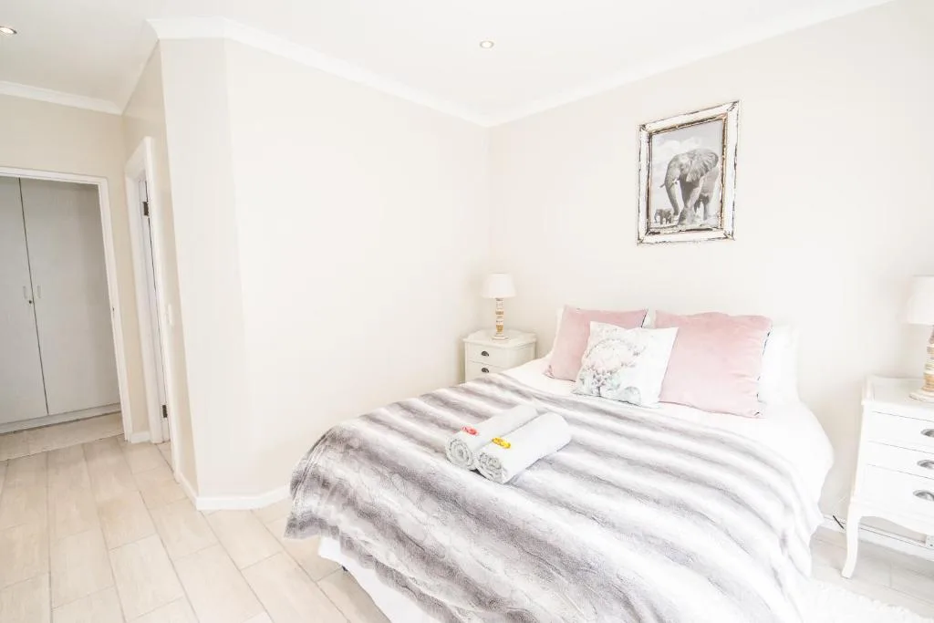 Bright bedroom with striped bedding, pink pillows, and white furnishings