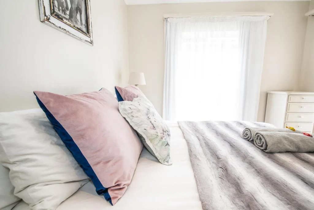 Bright bedroom with pink and blue pillows, striped blanket, and white curtains