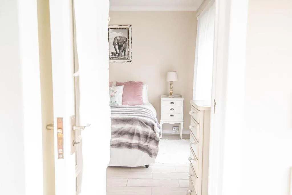 Bright bedroom with single bed, pink cushions, bedside table and lamp