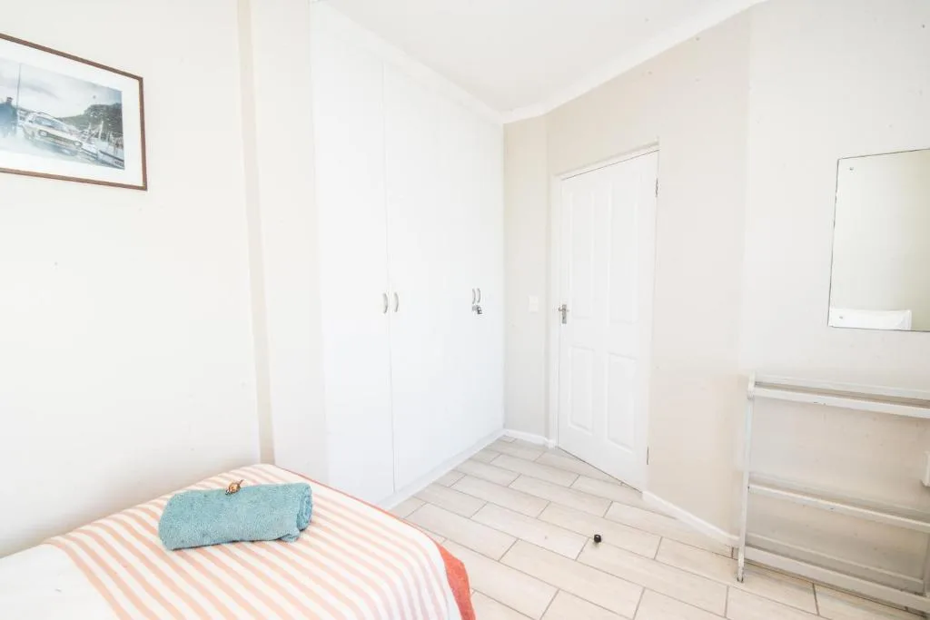 Bright bedroom with striped bedding, white built-in wardrobes, and mirror