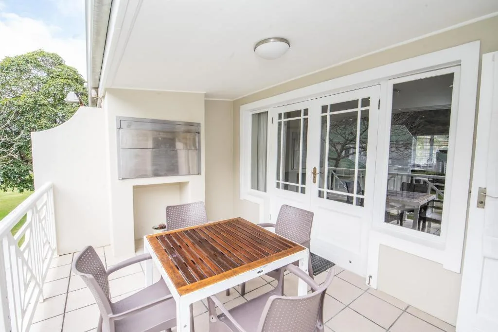 Covered patio with wooden dining table and four chairs overlooking garden