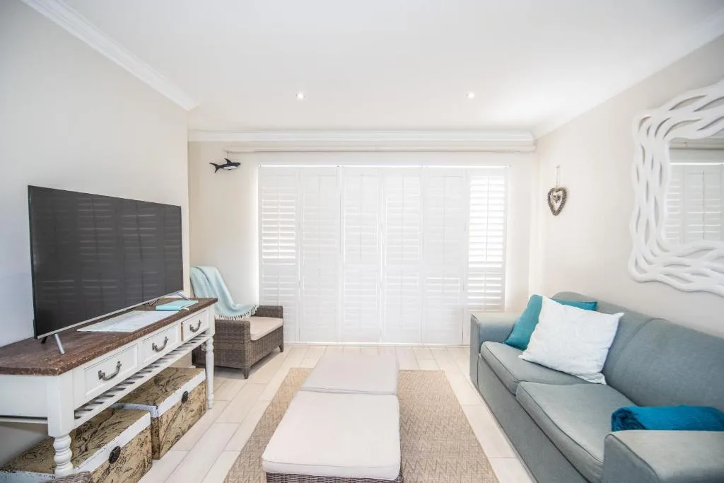 Bright lounge with grey sofa, TV on wooden stand, and ocean views through shutters