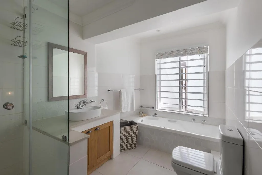 Bright bathroom with walk-in shower, vanity, bathtub, and louvered window