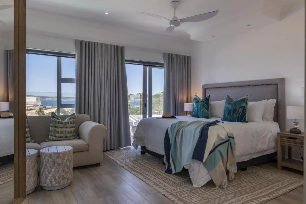 Spacious bedroom with king bed, ocean views through large windows, and coastal decor